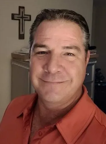 A man in an orange shirt smiling for the camera.