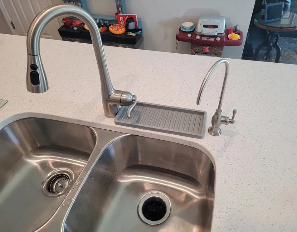 A kitchen sink with two faucets and a faucet that is connected to the counter.